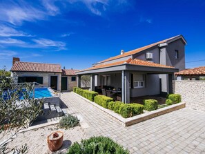 Une maison moderne à deux étages, dotée d’un patio couvert, d’une piscine et d’un jardin bien entretenu.