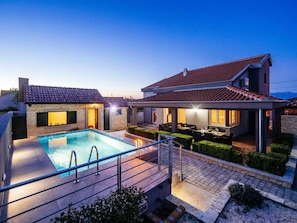 Ein Wohnhaus mit Swimmingpool, Sitzgelegenheit im Freien und einer überdachten Terrasse.