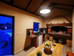 Une cuisine avec un four en briques, un coin repas avec une table et une vue sur une piscine.