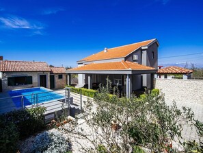 Ein modernes, zweistöckiges Haus mit Swimmingpool, Steinmauern und blauem Himmel.