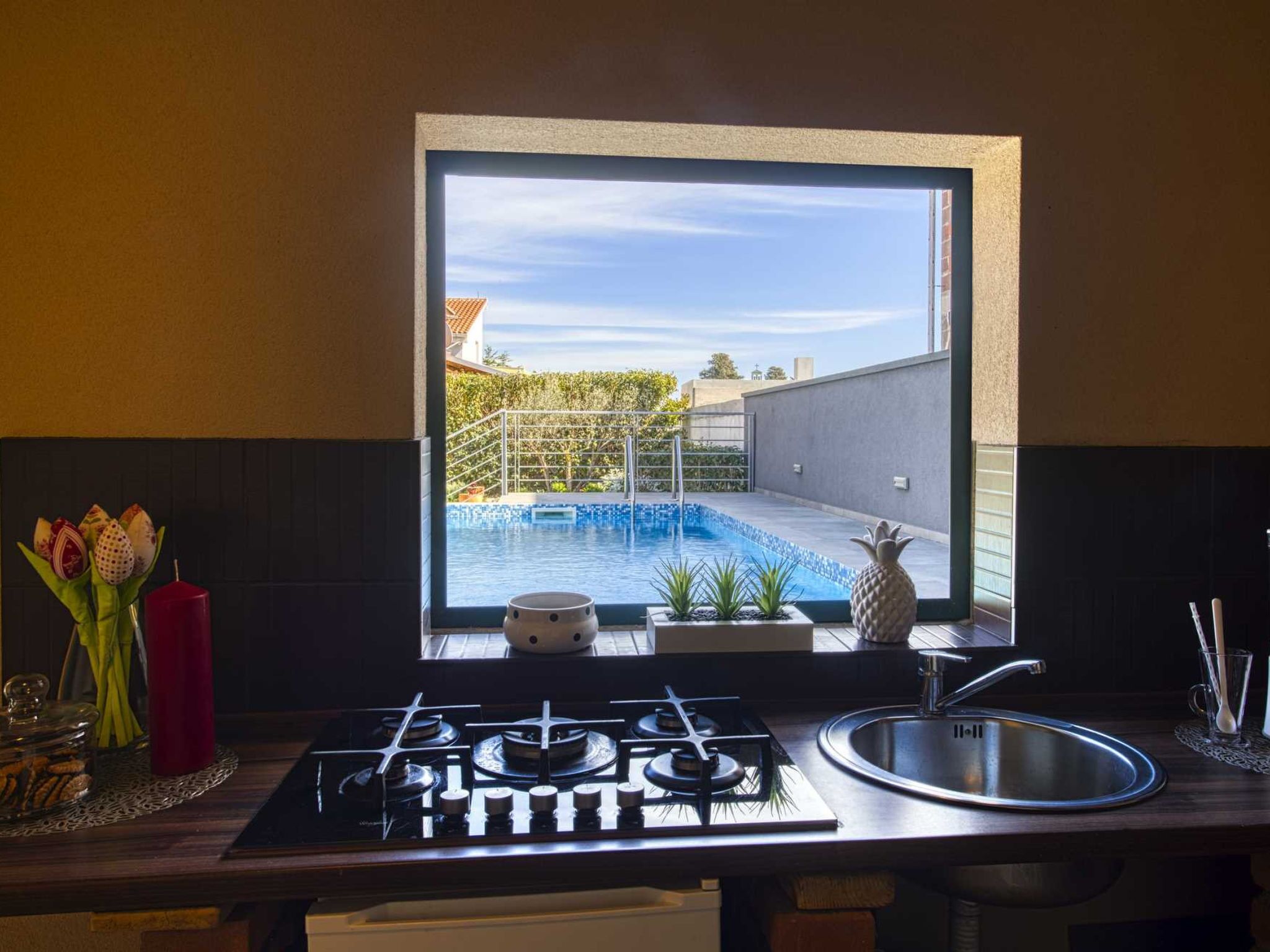 A kitchen with a view of a swimming pool, a gas stove, a sink, and decorative items.