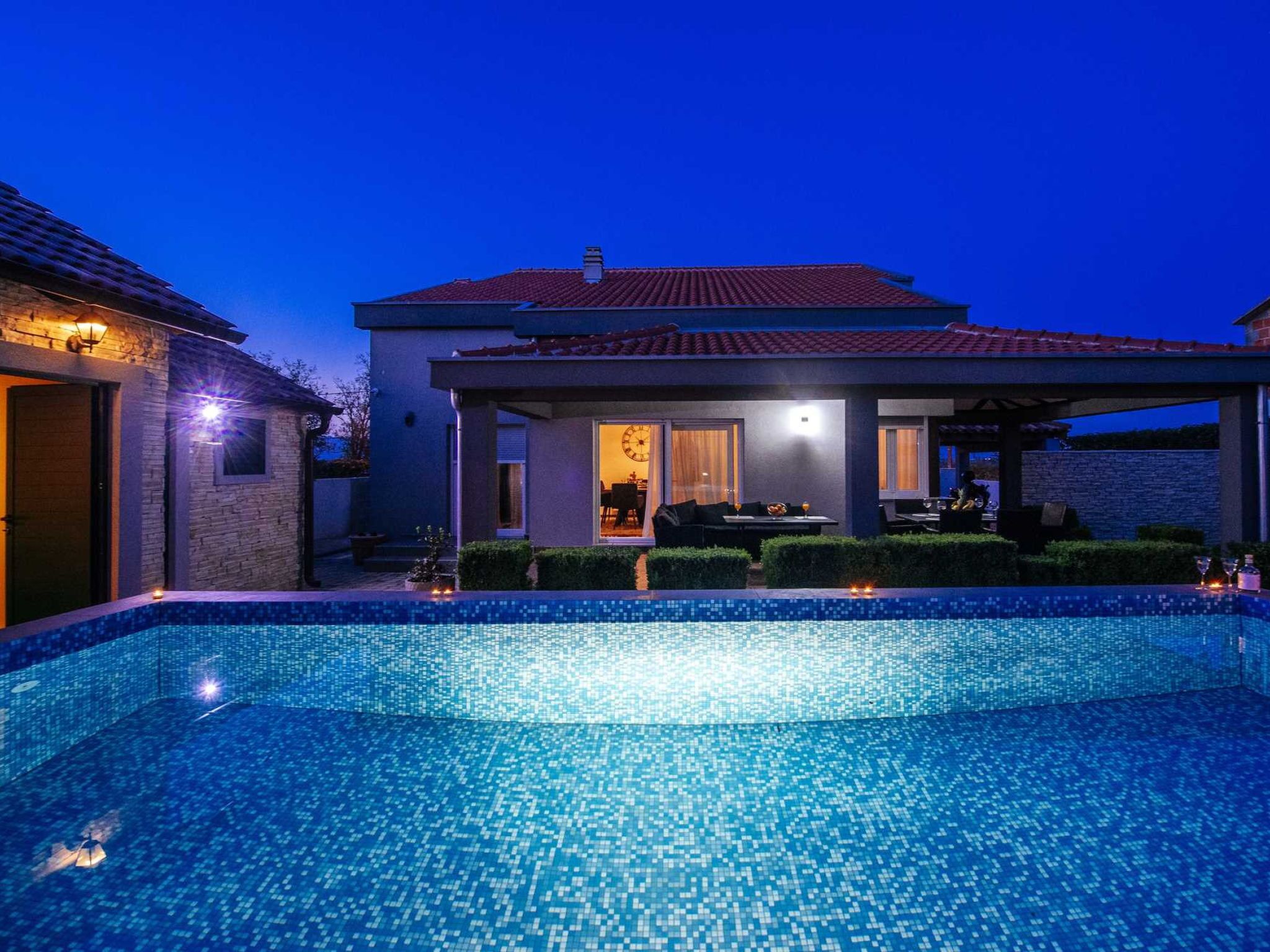 A modern house with a swimming pool, a covered patio, and a well-lit interior.