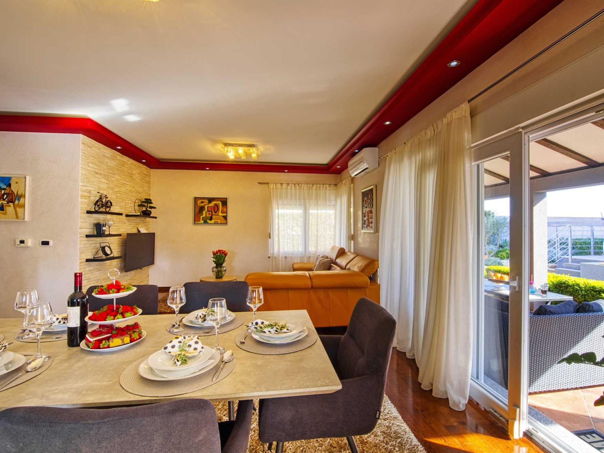 Un comedor con una mesa dispuesta para cuatro personas, un sofá y un amplio ventanal con cortinas.