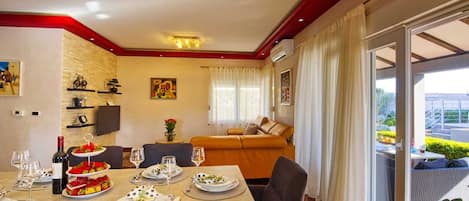 Un comedor con una mesa dispuesta para cuatro personas, un sofá y un amplio ventanal con cortinas.