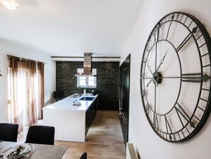 Eine moderne Küche mit Steinrückwand, einer zentralen Kochinsel und einer großen Wanduhr.