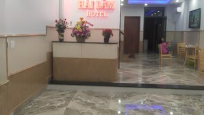 Zona de recepción de un hotel con piso de mármol, un mostrador de recepción con arreglos florales y un letrero de neón para HÀI LÀM HOTEL.