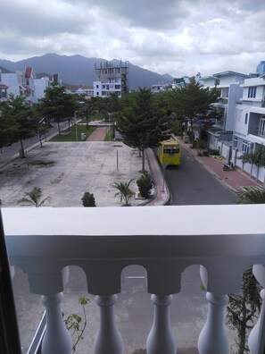 A yellow bus on a city street with modern buildings and a mountain in the background. - Hai Lam Hotel (Nha Trang)