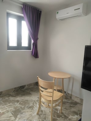 A room with a window, purple curtains, a wooden chair, a small round table, and a wall-mounted air conditioning unit. - Hai Lam Hotel (Nha Trang)