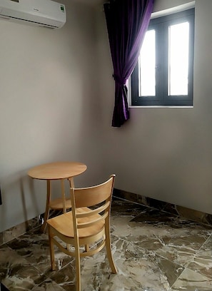 Una stanza con un piccolo tavolo in legno e una sedia, una finestra con tende viola e un condizionatore d'aria a parete.