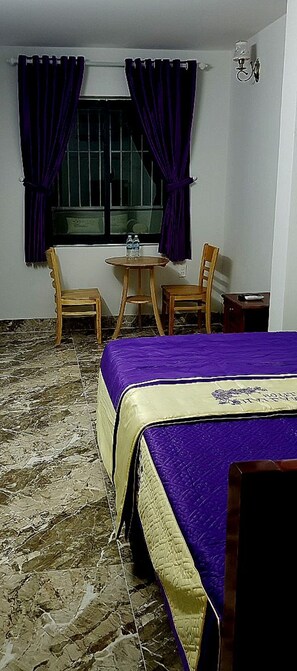 A room with a bed, a small table, two chairs, a window with curtains, and a wall-mounted light fixture. - Hai Lam Hotel (Nha Trang)