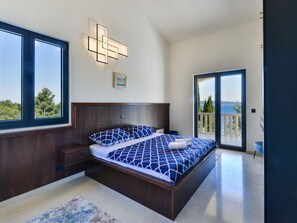 Ein Schlafzimmer mit einem großen Bett, einem Nachttisch, einer Wandleuchte und Blick durch eine Glastür.