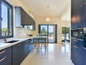 A modern kitchen with dark cabinetry, a stainless steel sink, and a dining area with bar stools. - Beachfront Villa Mediterranea with pool by Interhome (Ugljan/Kukljica)