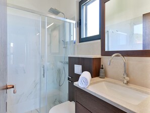 Ein modernes Badezimmer mit Duschkabine aus Glas, einem Waschbecken mit Spiegel darüber und einem Handtuch auf der Ablagefläche.