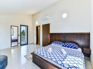 Een slaapkamer met een groot bed, een houten hoofdbord, een nachtkastje en een deur naar een balkon.