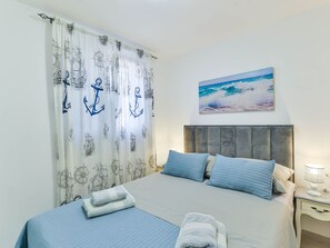 Quarto de hotel com uma cama, um quadro do oceano e cortinas com motivos náuticos.