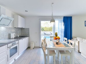 Uma cozinha moderna com armários brancos, forno embutido e uma área de refeições com mesa e cadeiras de vidro.