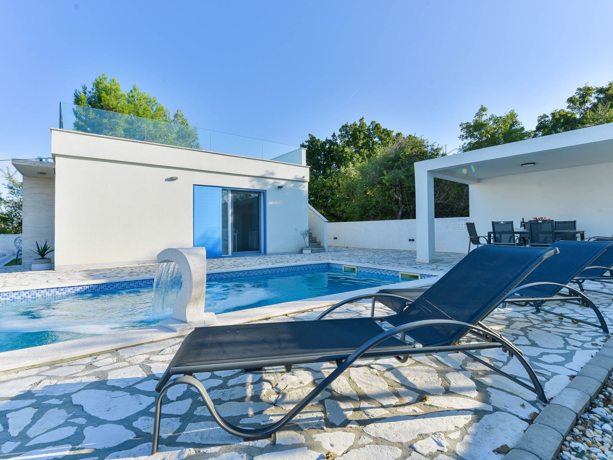 Un espace piscine extérieur moderne, doté de chaises longues et d’un petit bâtiment avec une porte bleue.