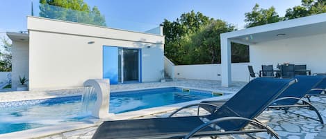 A modern outdoor pool area with lounge chairs and a small building with a blue door.
