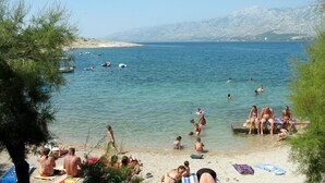 Ein Strand mit badenden Menschen, Booten im Wasser und Bergen im Hintergrund.