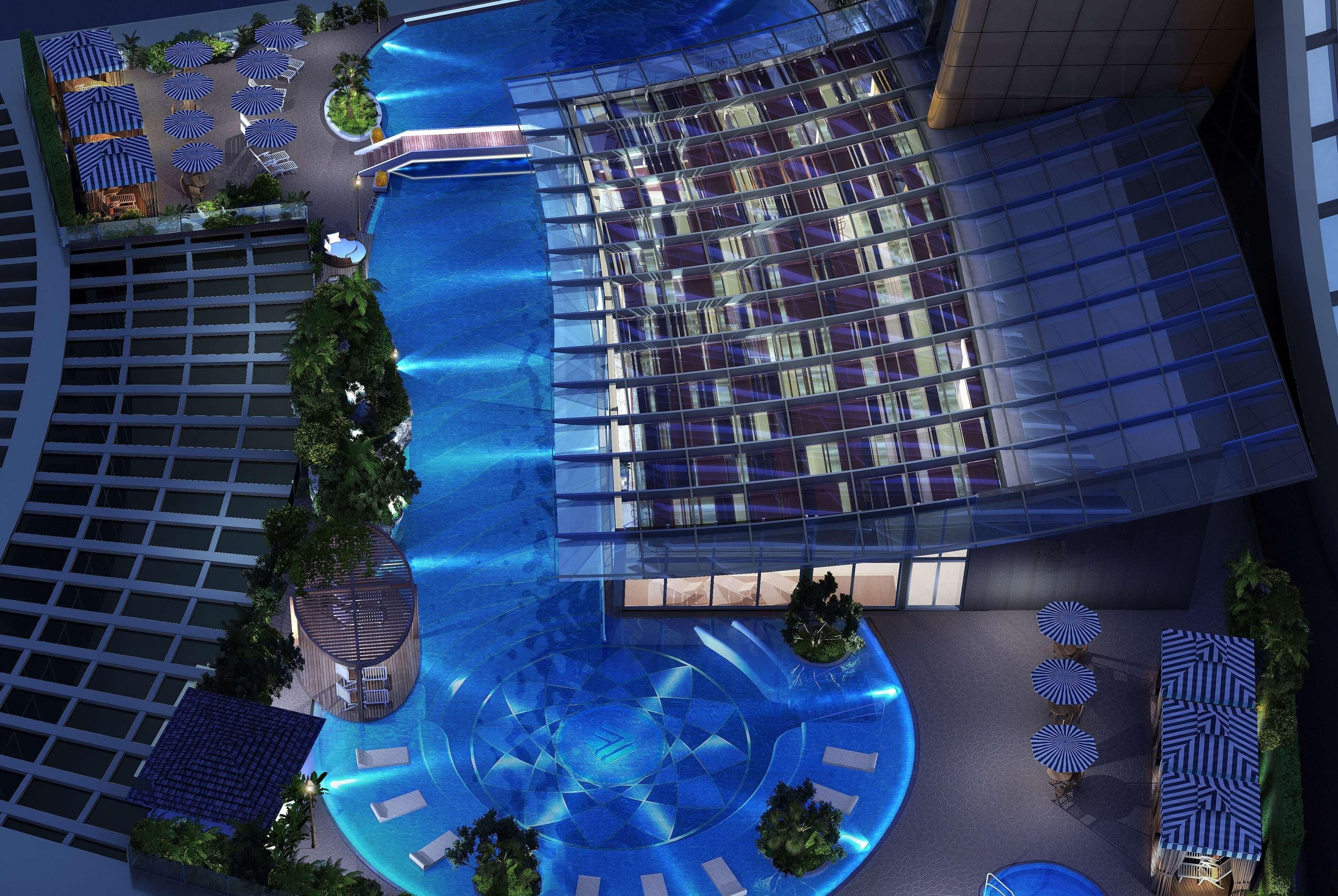 A modern hotel with a rooftop pool, sun loungers, and a glass facade.
