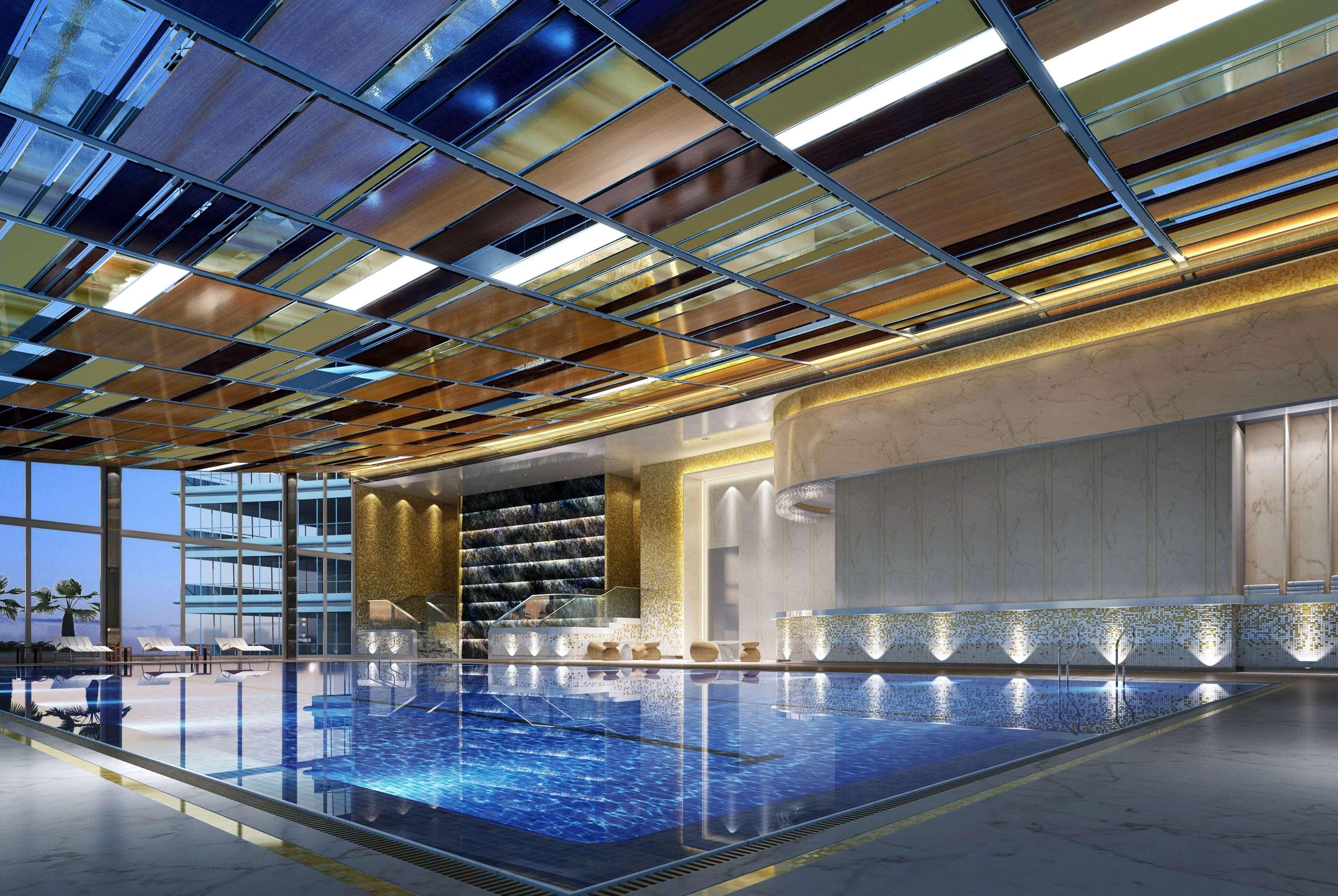 A modern indoor swimming pool with a glass ceiling and a view of a high-rise building.