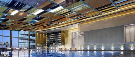 A modern indoor swimming pool with a glass ceiling and a view of a high-rise building.