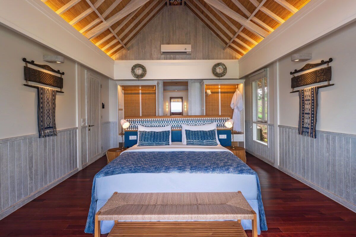 A spacious bedroom with a large bed, wooden ceiling beams, and a view of the outdoors.