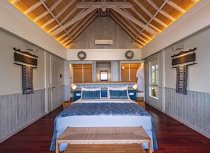 A spacious bedroom with a large bed, wooden ceiling beams, and a view of the outdoors.