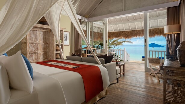 A bedroom with a bed, a wooden floor, a balcony with a view of the sea, and a thatched roof. - Sudamala Resort, Seraya (Labuan Bajo)