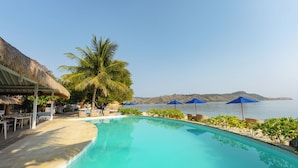 A poolside area with a thatched-roof structure, lounge chairs, and umbrellas. - Sudamala Resort, Seraya (Labuan Bajo)