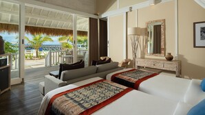 A hotel room with a large sliding glass door leading to a balcony, a bed with a patterned throw, a wooden dresser, and a mirror with a decorative frame. - Sudamala Resort, Seraya (Labuan Bajo)