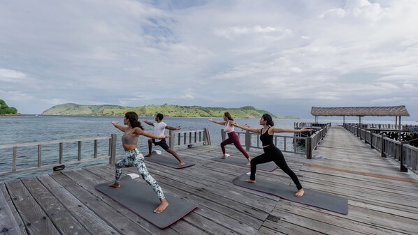 A wooden pier extending over water with people practicing yoga on mats. - Sudamala Resort, Seraya (Labuan Bajo)