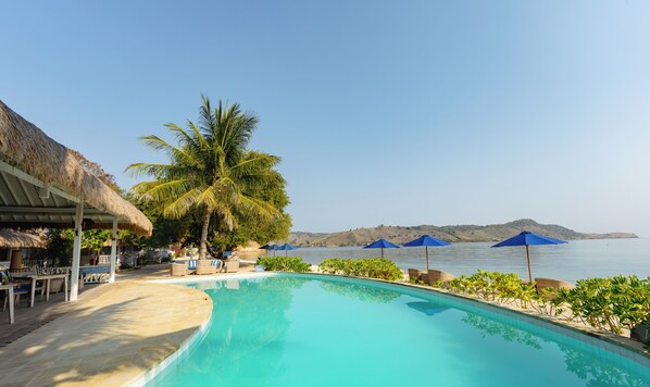 A poolside area with a thatched-roof structure, lounge chairs, and umbrellas. - Sudamala Resort, Seraya (Labuan Bajo)