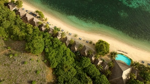 An aerial view of a beach resort with thatched-roof huts, a swimming pool, and a clear view of the turquoise sea. - Sudamala Resort, Seraya (Labuan Bajo)
