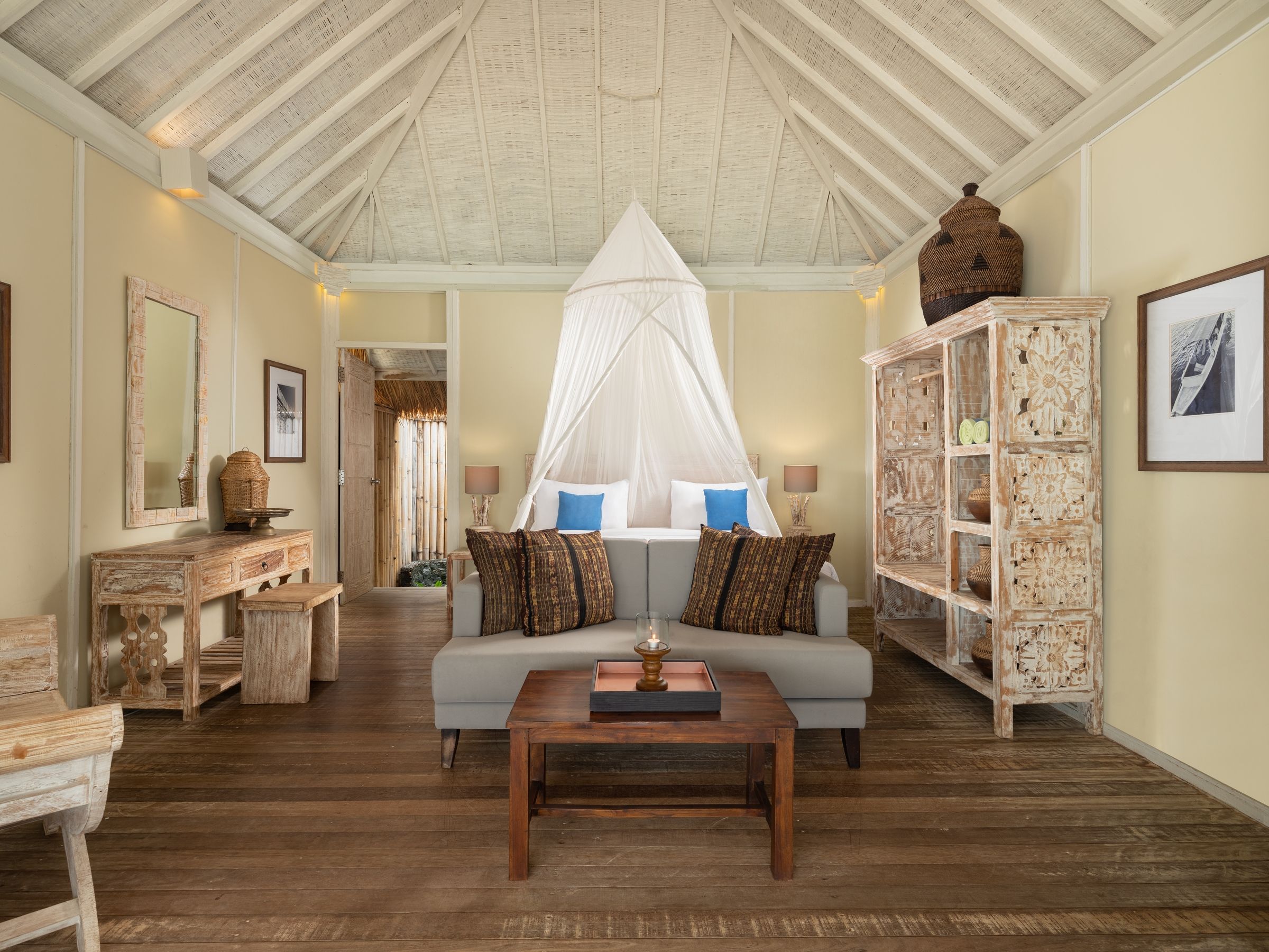 A room with a high ceiling, a canopy bed, a wooden cabinet, and a console table.