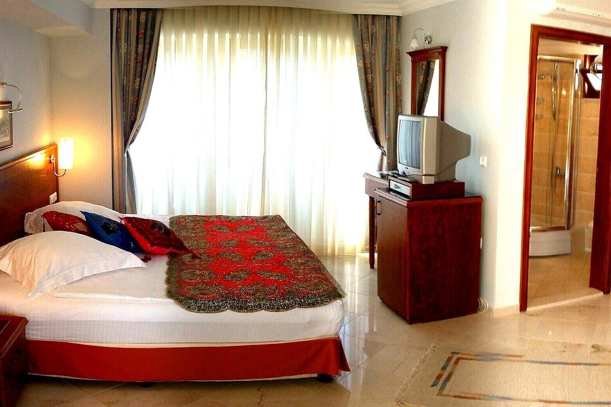 A hotel room with a bed, a TV, a desk, and a shower.