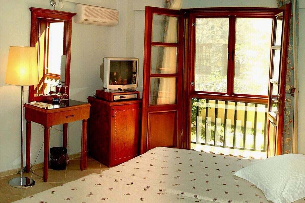 Ein Hotelzimmer mit einem Bett, einem Sessel, einem Schreibtisch mit Fernseher, einem Fenster mit Aussicht und einer Lampe.