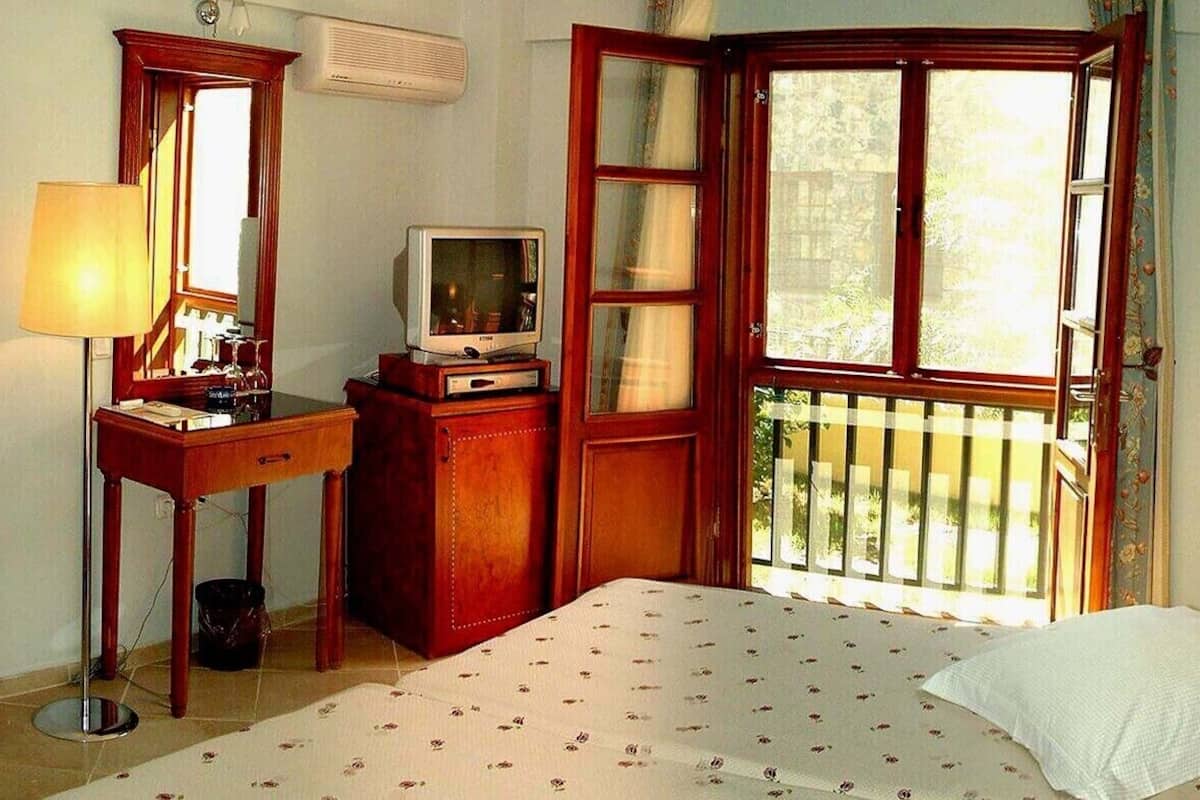 A hotel room with a bed, a chair, a desk with a television, a window with a view, and a lamp.