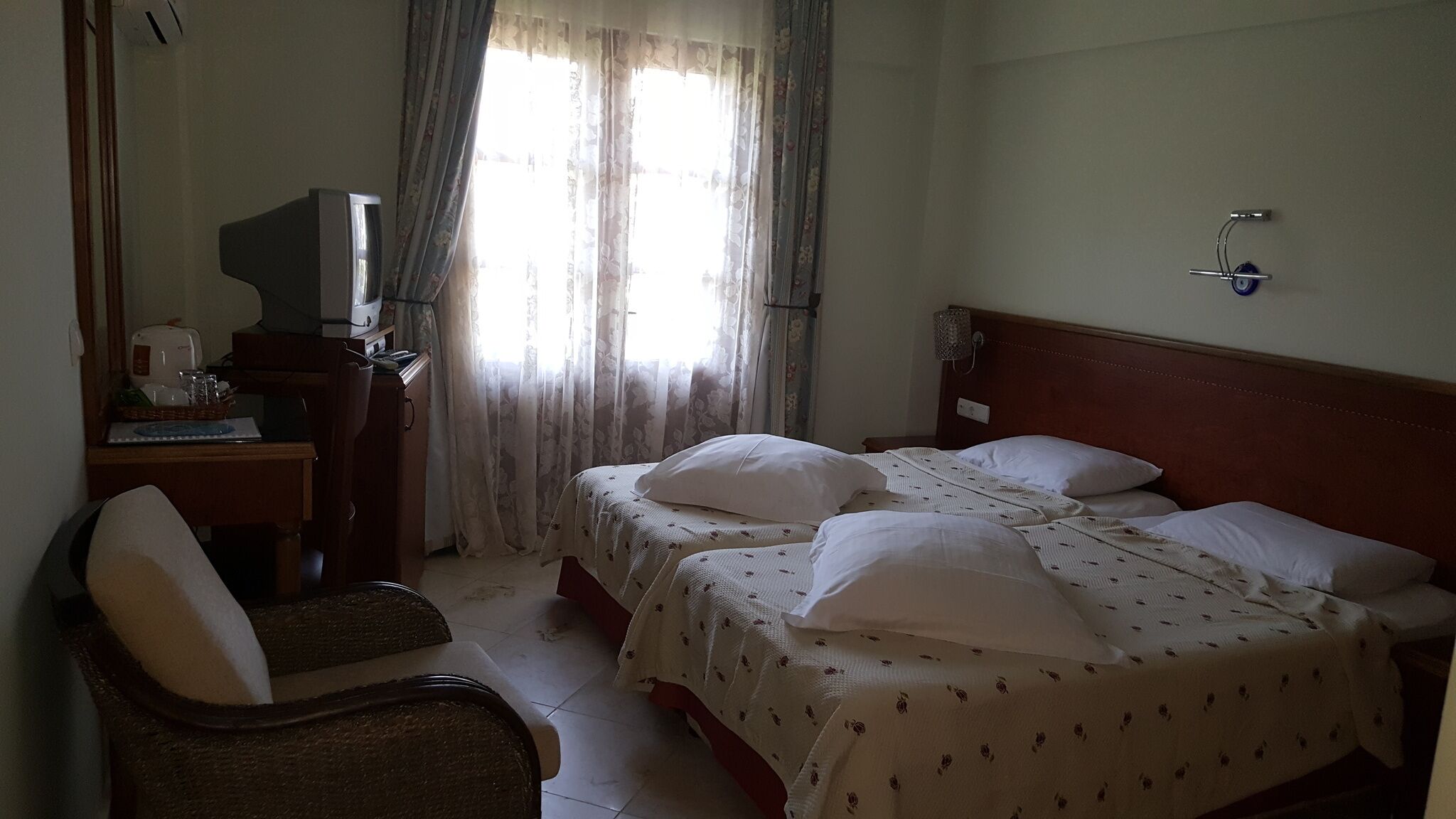 A hotel room with two beds, a desk with a television, a chair, and a window with curtains.