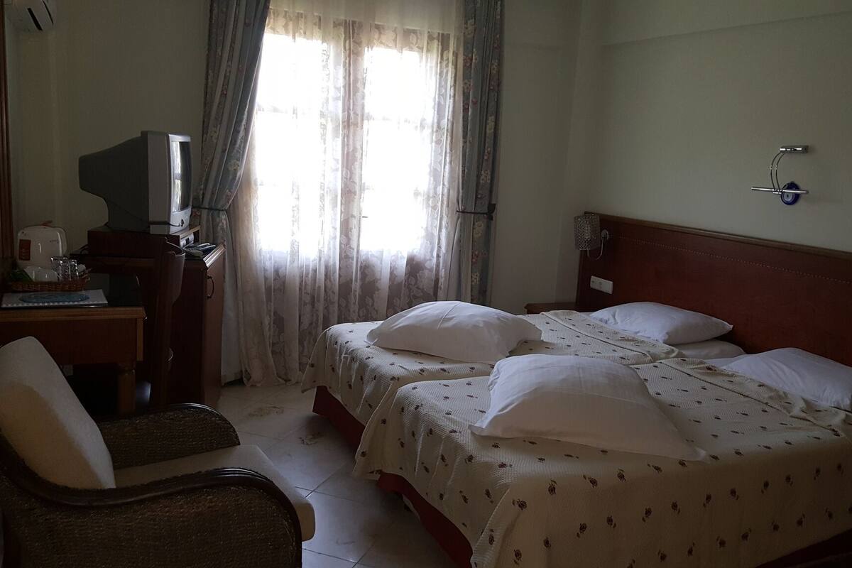 Ein Hotelzimmer mit zwei Betten, einem Schreibtisch, einem Fernseher, einem Sessel und einem Fenster mit Vorhängen.