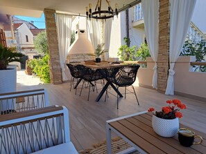 Um pátio externo com mesa e cadeiras, luminária pendente e plantas em vasos.