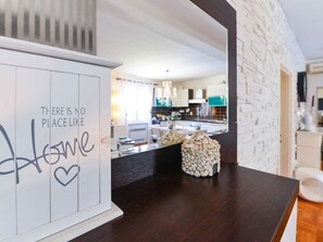 Un interior moderno con un mostrador de recepción de madera, una pared decorativa con un mensaje y una vista parcial de una cocina al fondo.