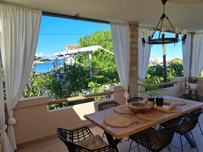 A dining area with a view of a coastal landscape, featuring a table with woven placemats, black chairs, and a hanging light fixture. - Modern Holiday house Gatsby only 40m from the sea by Interhome (Petrčane)