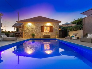Uma casa com piscina, fachada de pedra e área de estar externa.