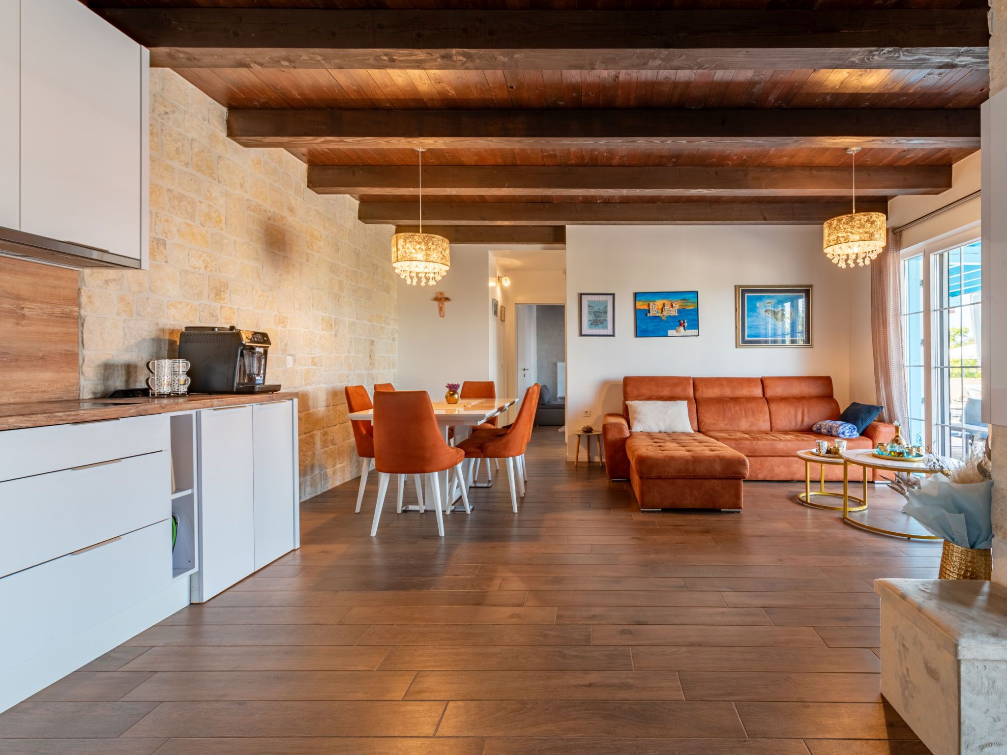 Eine moderne Küche mit Steinwand, Holzboden und einem Essbereich mit orangefarbenen Stühlen.