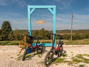 Deux vélos sont garés devant une structure bleue ornée d’une enseigne en bois, le tout étant entouré de verdure et se dressant sous un ciel dégagé.