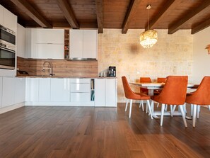 A modern kitchen with white cabinets, a wooden countertop, and a stone wall. There is a dining area with orange chairs and a white table. - Villa Jurenda with heated pool by Interhome (Debeljak)