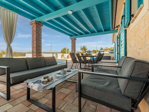 Une terrasse extérieure avec un plafond bleu, une piscine et des espaces aménagés pour s’asseoir.