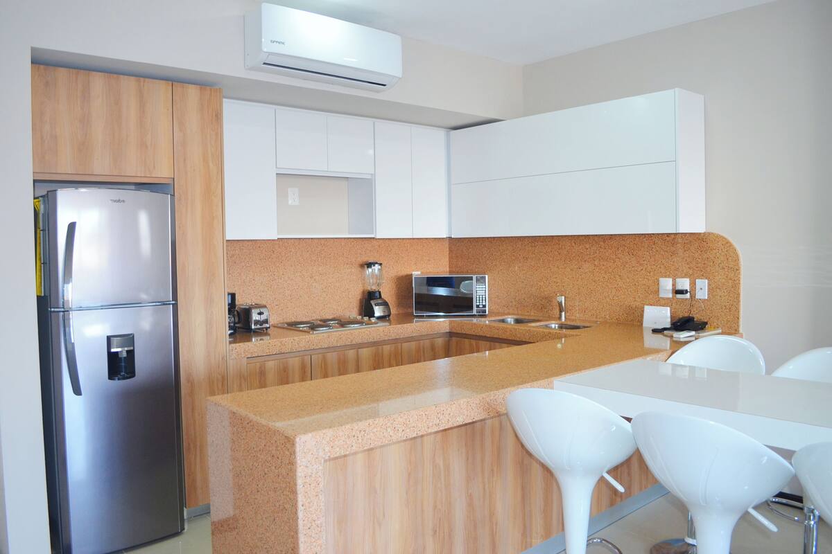 Una cocina moderna con un refrigerador de acero inoxidable, un microondas, una licuadora y un lavamanos.