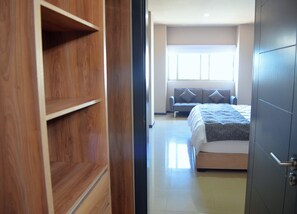 Quarto com cama, sofá cinza e guarda-roupa de madeira.
